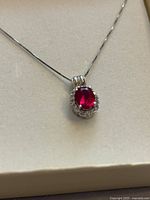 Close-up of pendant showing red oval stone, halo accents, and chain attachment