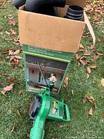 Retail box opened showing tube sections and separate blower housing on grass