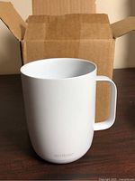 Front view of white Ember Mug 2 in front of open box