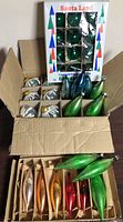 Overall lot view showing boxed green balls, silver ribbed ornaments, elongated drops in two boxes