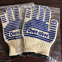 Pair of cream cotton oven gloves in plastic packaging, blue grip stripes visible