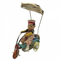 Side view of tin wind-up tricycle showing rider, canopy, wheels