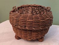 Round Indigenous woven basket on bun feet, side view showing body weave