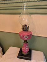 Full view of pink floral glass oil lamp with chimney on black base