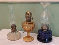 Three miniature oil lamps: clear ribbed, amber pedestal, cobalt blue, showing overall condition and presence or absence of chimneys