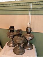 Front view of three nickel oil lamps, one with glass chimney