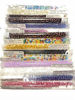 Stack of 15 clear plastic tubes filled with assorted seed beads, showing colours and price labels