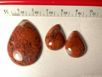 Front view of three polished red brecciated jasper teardrop cabochons beside ruler for scale
