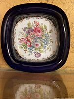 Top-down view of square porcelain dish with floral center and cobalt rim