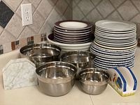 Assorted bowls, plates, stainless mixing bowls, marble and rooster napkin holders grouped on counter