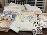 Stacks of assorted linens laid out, showing embroidery, floral, fruit, geometric and holiday prints, plus quilted pads