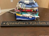 Stack of folded aprons and tea towels with wooden Grandma’s Kitchen sign in foreground
