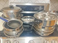 Stacked assortment of stainless pans, steamer inserts, egg-poacher insert, lids