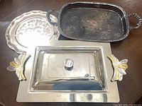 All four trays grouped: stainless with gold accents, lidded tray, tarnished gallery tray, round tray