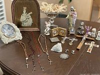 overall lot layout on table showing rosaries, framed images, statues, medals, crucifixes, bag of beads