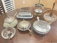 Group shot of all seven silverplate and glass condiment pieces with spoons displayed on table