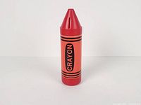 Front view of red plastic crayon coin bank showing CRAYON label and slot on tip