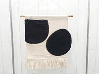 Full view of beige tapestry with black shapes, dowel, and cord