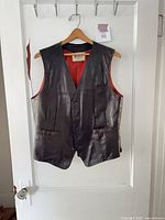 Full view of brown leather vest on hanger showing front, buttons, pockets, red lining edges