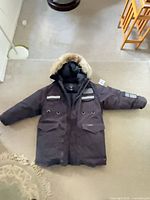 Full view of navy Canada Goose parka laid flat showing overall design, pockets, reflective trim, hood fur.