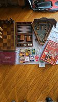 Overview of all items laid out: chess board with pieces, backgammon board open, Circa Baseball game, Trivial Pursuit card set box, playing card decks