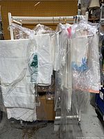 Multiple white embroidered tablecloths and bagged linens hanging on rack