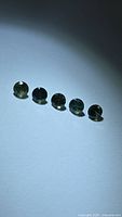 Five loose round green sapphires lined up on light background