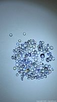 Scattered round diamond-cut tanzanite gemstones under direct light showing color range and sizes