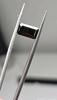 Green octagon-cut tourmaline held in tweezers, showing shape and color