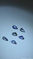 Six pear-cut tanzanites on neutral background, showing color and clarity
