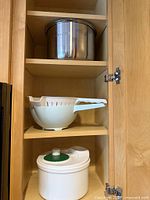 Cabinet shelves showing stainless steel stockpot, white colander, white salad spinner