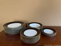 Four stacks of Daniel Hechter Venetian Ebony plates of varying sizes on a wooden surface