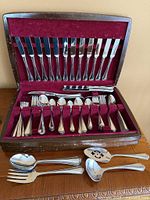 Open wooden chest showing complete flatware service and additional serving spoons