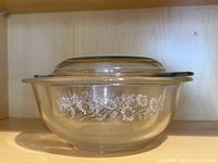 Side view of clear Pyrex bowl showing white floral pattern and lid on top