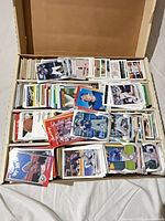 Open five-row card storage box filled with assorted MLB trading cards; loose cards on top show various designs