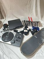 All items laid out: PS3 console, cords, DJ Hero turntable, Tony Hawk Ride board, controllers, EA Active sensors, stack of game cases