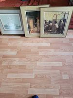 All three framed prints leaning against sofa on hardwood floor