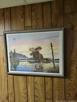Framed moose wildlife print hanging on paneled wall, shows full framed artwork