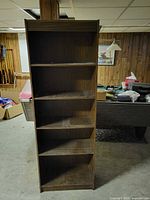 Front view of tall narrow dark brown laminate bookcase showing five fixed shelves and top surface
