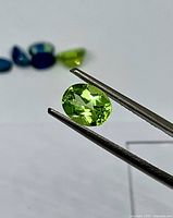 Oval peridot held in tweezers showing color and cut