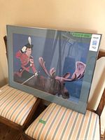 Full view of framed Charles Pachter print resting on chairs