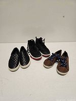 Three pairs of kids shoes laid out: black quilted slip-ons, black athletic sneakers, brown sneakers