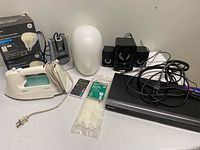 Group shot of all items including Philips iron, clock radio, lamp shade, speaker set, GE smart bulb boxes, calculator, zip ties, Sony DVD player with cables