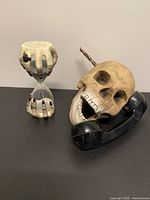 Overview of both items on black surface: skeleton hand hourglass and skull telephone prop
