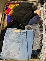 Open suitcase showing folded clothing including denim jeans and assorted garments