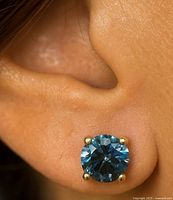 Blue lab diamond stud worn in ear, shows size and four-prong yellow gold setting