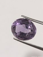 Front view of faceted oval amethyst held by tweezers