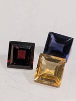 Front view of three square-cut gemstones in red, yellow, blue
