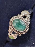 Top view of silver ring showing emerald cabochon, rope bezel, accent stones