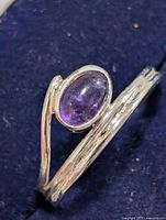 Wrap-style silver ring with oval amethyst cabochon set on dark background